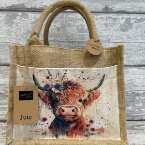 K&ouml;nnte beinhalten: Eine braune Jute-Tragetasche mit einem Blumendesign, das eine Highland-Kuh zeigt. Die Tasche hat ein braunes Papieretikett mit der Aufschrift "Westford Mill" und "Jute". Ein kleines braunes Papieretikett in Kreisform lautet "Handmade with love".
