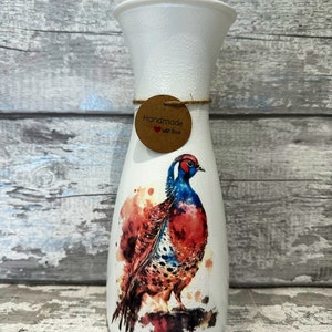 May include: White ceramic vase with a watercolor painting of a pheasant on it. The vase has a brown tag that says "Handmade with Love".