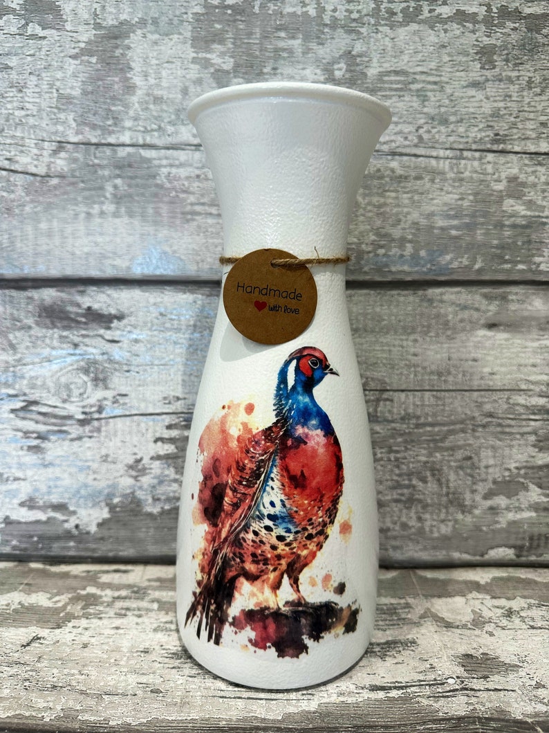 May include: White ceramic vase with a watercolor painting of a pheasant on it. The vase has a brown tag that says "Handmade with Love".