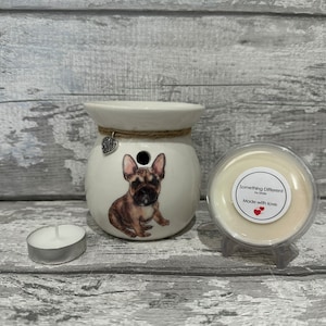 Peut inclure: Un brûleur de cire en céramique blanche avec une illustration de bouledogue français marron et beige. Le brûleur a un détail de corde de jute et un petit charme en forme de cœur. Une bougie chauffe-plat et un contenant de cire sont également présents.