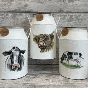 Peut inclure: Trois bidons en métal blanc avec des motifs de vaches différents. Les bidons sont décorés de vaches noires et blanches et du texte "Handmade with love".