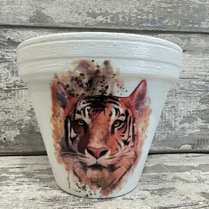 May include: White ceramic planter featuring a watercolour design of a tiger's face. The tiger has orange and black stripes and a brown nose.