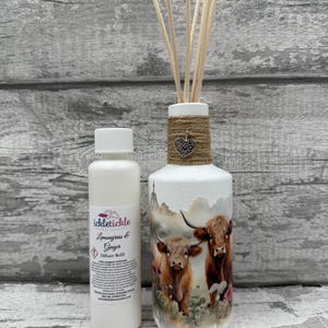 Peut inclure: Un diffuseur blanc avec un motif de vache Highland, des détails en ficelle et des bâtonnets en bois. Une bouteille de recharge avec le texte "Lemongrass & Ginger" est à côté. Article de parfum d'intérieur.
