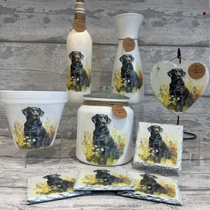 May include: A set of home decor items featuring a black Labrador Retriever design. The set includes a vase, a bottle, a jar, a planter, a heart-shaped plaque, and four coasters. All items are white with a black Labrador Retriever design and the words "Handmade with Love".