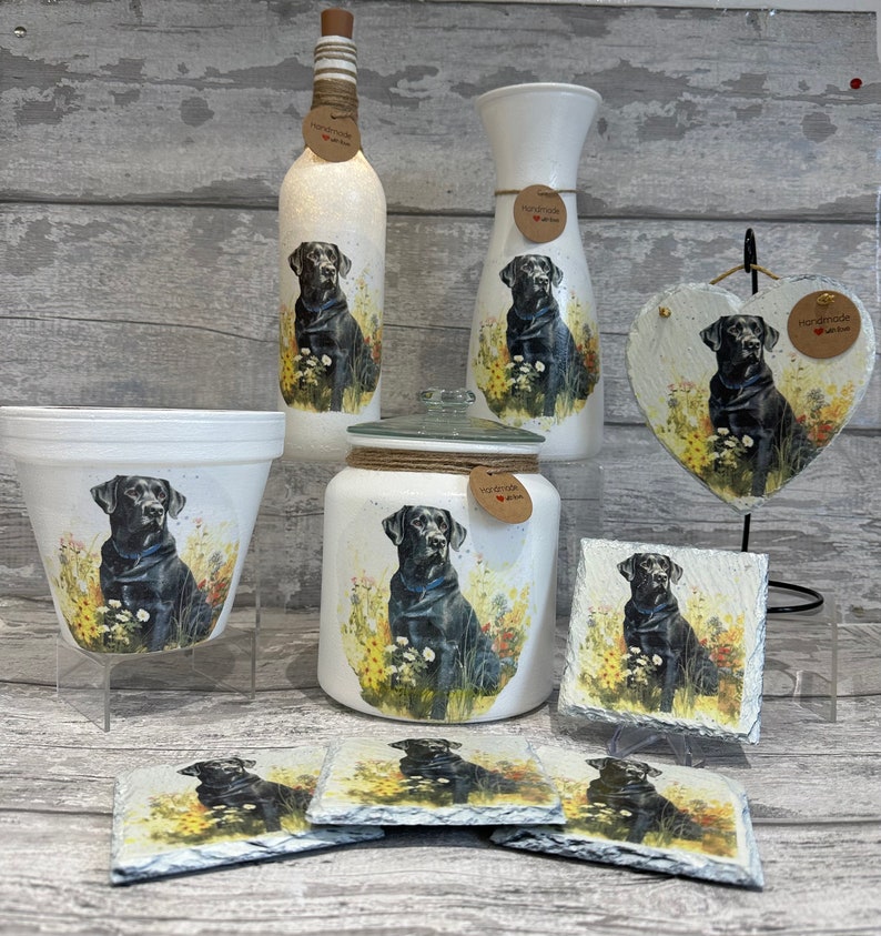 May include: A set of home decor items featuring a black Labrador Retriever design. The set includes a vase, a bottle, a jar, a planter, a heart-shaped plaque, and four coasters. All items are white with a black Labrador Retriever design and the words "Handmade with Love".