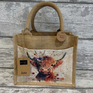 K&ouml;nnte beinhalten: Eine braune Jute-Tragetasche mit einem Blumenmuster einer Highland-Kuh. Die Tasche hat eine Tasche auf der Vorderseite und ein braunes Etikett mit der Aufschrift "Handmade with love".