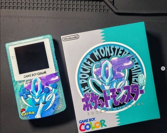 以下が含まれることがあります： 水色のGame Boy Colorコンソールと、Suicuneのデザインとマッチする箱。箱には「THE POCKET MONSTER」の文字と日本語の文字が書かれています。コンソールには黒い画面と任天堂のロゴがあります。