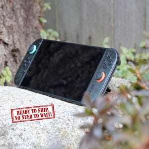 May include: A black handheld gaming console with attached controllers. The controllers have teal and orange accents. The screen is black. The text "READY TO SHIP, NO NEED TO WAIT!" is printed on a red stamp.