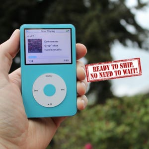 Może przedstawiać: Turkusowy iPod trzymany w dłoni, wyświetlający ekran "Now Playing" ze szczegółami piosenki: "Gethsemane", "Sleep Token" i "Even In Arcadia". Urządzenie posiada okrągły panel sterowania i ekran pokazujący postęp utworu. Obraz zawiera tekst "READY TO SHIP, NO NEED TO WAIT!"