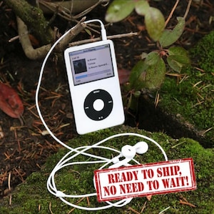 May include: White iPod music player with a black control wheel and white earbuds. The screen displays a song title. The text "READY TO SHIP, NO NEED TO WAIT!" is on a red sign.