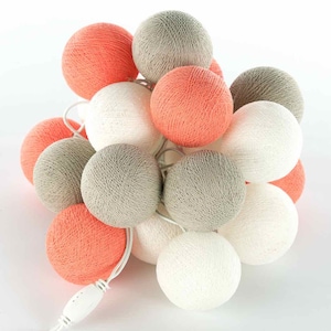 Könnte beinhalten: Eine Lichterkette aus Baumwollkugeln mit einem Mix aus weißen, grauen und korallenfarbenen Kugeln. Die Lichter sind mit einem weißen Kabel verbunden und haben einen weißen Stecker.