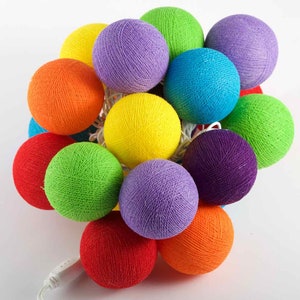 Pode incluir: Uma corda de 12 luzes de bolas de algodão em um arco-íris de cores, incluindo vermelho, laranja, amarelo, verde, azul, roxo e branco. As luzes são conectadas por um fio branco e cada bola de algodão tem uma lâmpada transparente.