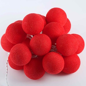 Op de afbeelding: Een string met rode katoenen ballenlampjes. De lampjes zijn in een tros gerangschikt, waarbij sommige ballen elkaar overlappen. De lampjes zijn aan een wit snoer bevestigd.