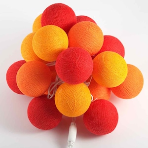 Könnte beinhalten: Eine Lichterkette aus Baumwollkugeln mit einer Mischung aus roten und orangen Kugeln. Die Lichter sind mit einem weißen Kabel mit Stecker verbunden.