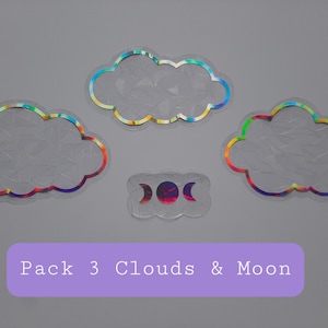 Puede incluir: Un paquete de tres pegatinas de nubes holográficas iridiscentes y una pegatina de luna holográfica iridiscente. Las pegatinas están sobre un fondo gris. Pack 3 Clouds & Moon.