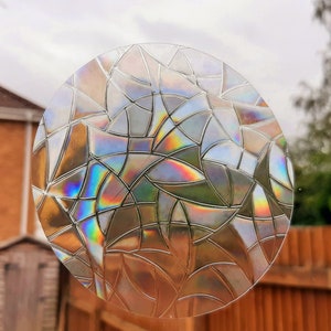 Könnte beinhalten: Eine runde, transparente, irisierende Fensterfolie mit einem geometrischen Muster aus überlappenden Blättern. Die Folie hat einen Glasmalerei-Effekt und erzeugt einen Regenbogen aus Farben.
