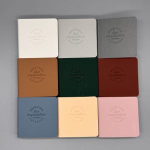 May include: Nine square notebooks in various colors, including white, gray, brown, green, red, blue, yellow, and pink. Each notebook cover features the embossed text "PAINTING Art Inspiration NOTEBOOK". The notebooks are arranged in a grid pattern.
