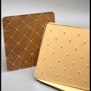 May include: Two square, decorative panels. One is a warm brown color, the other is a light gold. Both have a geometric pattern of intersecting lines and small, clear, round accents. The panels are likely for home decor or craft projects.