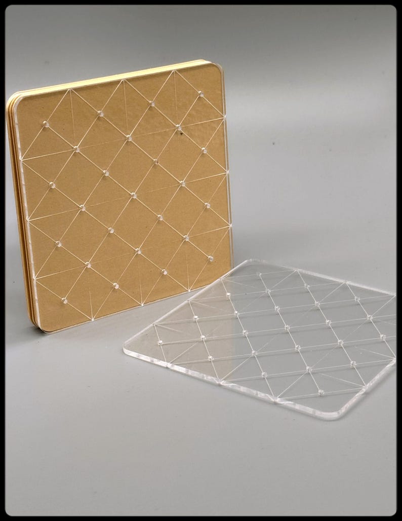 May include: A square, tan-colored notebook with a clear, grid-like design made of string and small beads. A separate, clear acrylic sheet with the same grid pattern is also present. The notebook is open, revealing the pages.