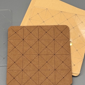 May include: A stack of square, brown paper cards with a geometric pattern of intersecting lines and dots. The cards are arranged on a gray surface, with a clear plastic template with a similar design visible in the background.