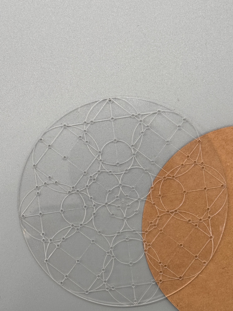 May include: Two clear, circular stencils with geometric designs. One stencil is transparent, and the other is a light brown color. The stencils are placed on a gray surface.