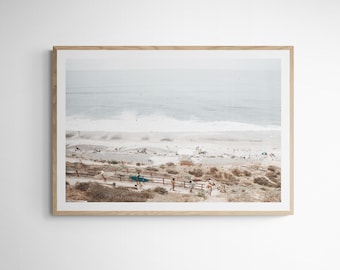 May include: An aerial view of a beach with a wooden walkway leading down to the sand. The ocean is in the background with waves crashing on the shore. There are people on the beach and in the water.