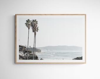 Puede incluir: Una fotografía enmarcada de una escena de playa con tres palmeras en primer plano y una vista brumosa de una costa en el fondo.