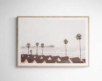 May include: A framed photograph of a beach scene with a row of houses in the foreground, a pier in the distance, and palm trees in the middle ground.