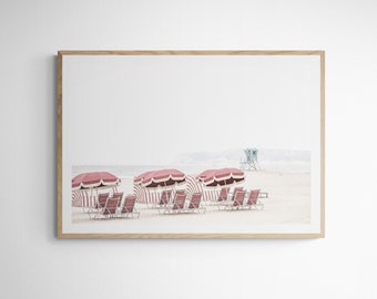 May include: A beach scene with red and white striped umbrellas and red lounge chairs on a white sandy beach. A blue lifeguard stand is in the background.