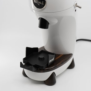 Puede incluir: Molinillo de café Niche Zero blanco con un portafiltro de plástico negro y una base de madera con el logotipo de Decent.
