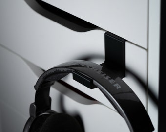 May include: Black headphones with a black hook hanging on a white drawer. The headphones have the word "Sennheiser" printed on the side.