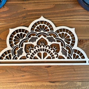 May include: A white wooden mandala design with intricate cutouts. The mandala is in the shape of a half circle and has a decorative border.