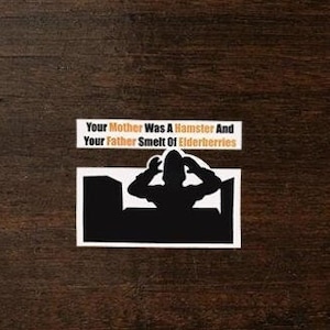 May include: A black and white sticker with a silhouette of a person with their hands over their head. The text on the sticker reads "Your Mother Was A Hamster And Your Father Smelt Of Elderberries."