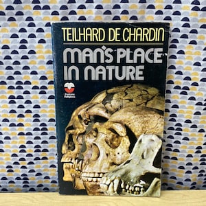 May include: A book titled "Man's Place in Nature" by Teilhard de Chardin. The cover features a close-up of several skulls.