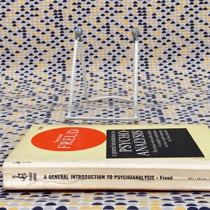 May include: A white metal book stand with a book titled "A General Introduction to Psychoanalysis - Freud" on top of it. The book cover is yellow with a red circle that says "Sigmund Freud" in white text.