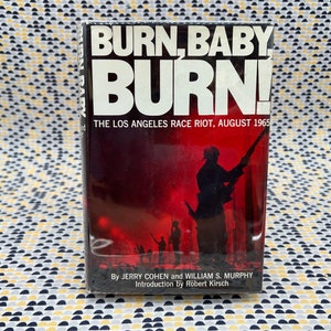 May include: A vintage paperback book titled "Burn, Baby Burn! The Los Angeles Race Riot, August 1965" by Jerry Cohen and William S. Murphy. The cover features a black and white photo of a man in a military uniform holding a rifle, with other figures in the background.
