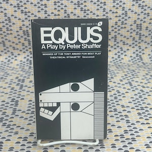 May include: A paperback book titled Equus, a play by Peter Shaffer. The black cover features white text and a stylized geometric horse head illustration. The text reads Winner of the Tony Award for Best Play and Theatrical Dynamite! Newsweek.