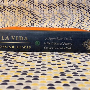 Op de afbeelding: Een blauw hardback boek getiteld "La Vida" door Oscar Lewis. De ondertitel van het boek is "Een Puerto Ricaanse familie in de cultuur van armoede - San Juan en New York". Het boek is uitgegeven door Random House.