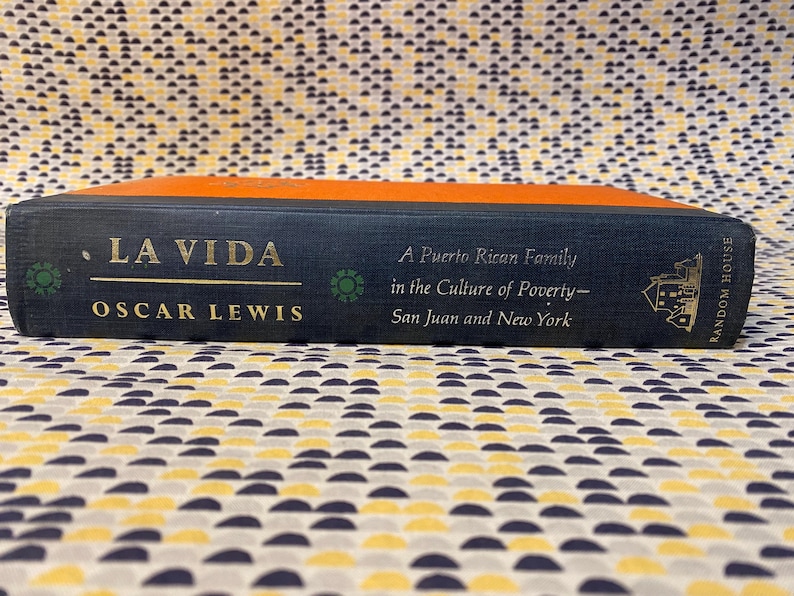 Op de afbeelding: Een blauw hardback boek getiteld "La Vida" door Oscar Lewis. De ondertitel van het boek is "Een Puerto Ricaanse familie in de cultuur van armoede - San Juan en New York". Het boek is uitgegeven door Random House.