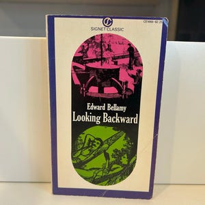 May include: A paperback book titled "Looking Backward" by Edward Bellamy. The cover has a purple border, a Signet Classic logo, and illustrations in pink, black, and green. The book's title is in bold, black font.
