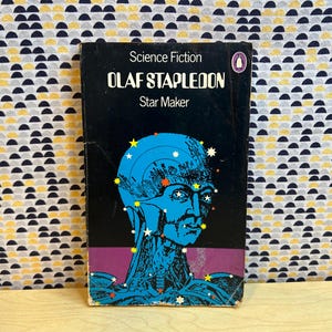 May include: A vintage paperback book titled "Star Maker" by Olaf Stapledon. The cover features a blue illustration of a human head with stars, set against a black background. The book is labeled "Science Fiction".