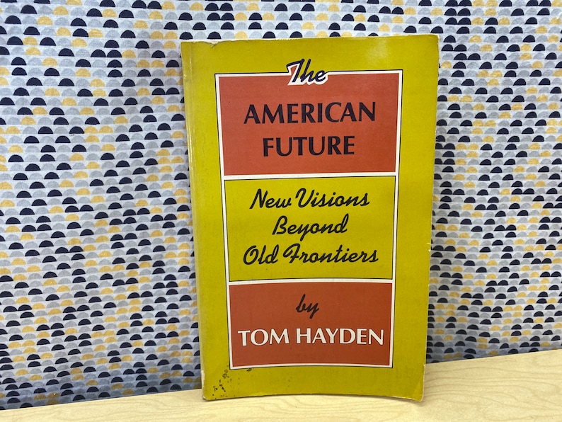 May include: A yellow and orange book titled "The American Future: New Visions Beyond Old Frontiers by Tom Hayden".