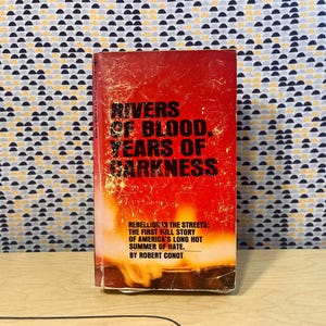May include: A vintage book titled "Rivers of Blood, Years of Darkness" with a red and orange cover. The book's cover features bold black text and the subtitle "Rebellion in the Streets: The First Kill Story of America's Long Hot Summer of Hate."
