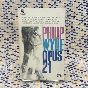 Op de afbeelding: Een vintage paperback boekomslag met een vrouwengezicht op de voorkant. De titel is "Philip Wylie Opus 21" en de tekst luidt "It shocks. The place is New York. The time is now. The cast-an author, a wife, a girl whose way of life makes her an outcast. Provocative Wylie's most startling book."