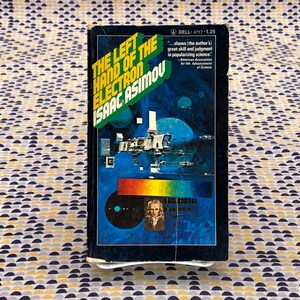 May include: A paperback book cover with a blue background and a space scene. The title is "The Left Hand of the Electron" by Isaac Asimov. The text on the cover reads "...shows the author's great skill and judgment in popularizing science." - American Association for the Advancement of Science.