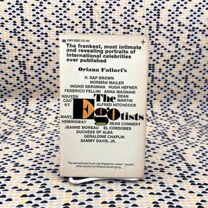 Puede incluir: Un libro de bolsillo vintage titulado "The Egotists" de Oriana Fallaci. La portada presenta una lista de celebridades y el texto "Tempo Books 5327 956". El fondo es una tela estampada con formas negras, blancas y amarillas.