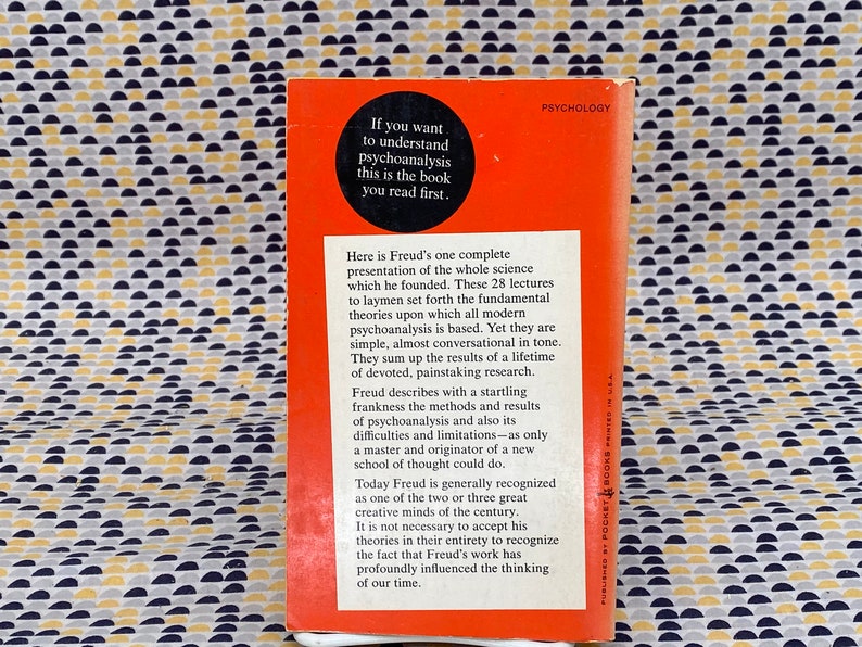 May include: A red paperback book with the title "Psychology" and the text "If you want to understand psychoanalysis this is the book you read first." on the cover. The back cover features a description of the book and its author, Sigmund Freud.
