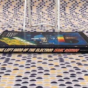 May include: A black paperback book titled "The Left Hand of the Electron" by Isaac Asimov. The cover features a colorful image of a space station and a rainbow.