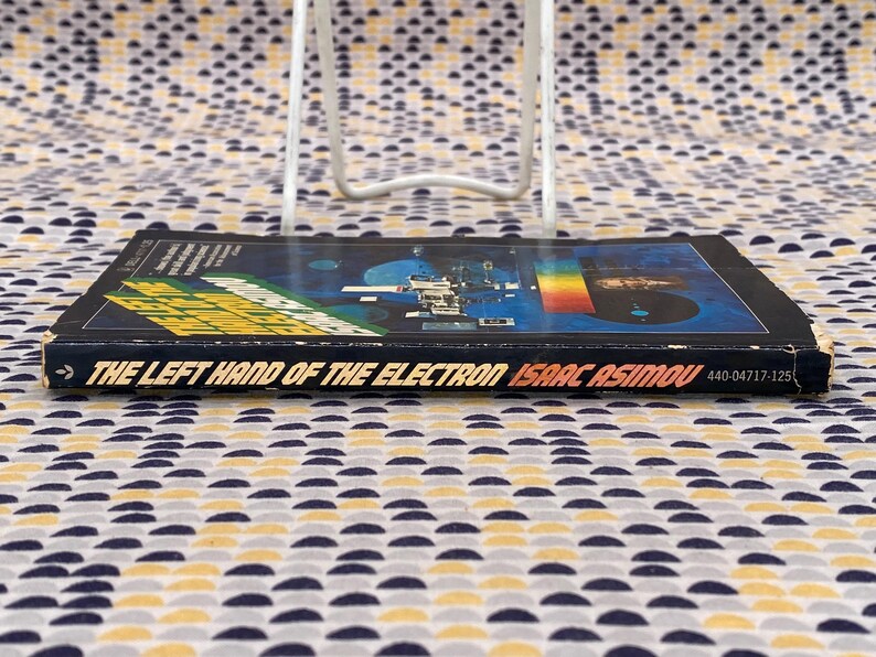 May include: A black paperback book titled "The Left Hand of the Electron" by Isaac Asimov. The cover features a colorful image of a space station and a rainbow.