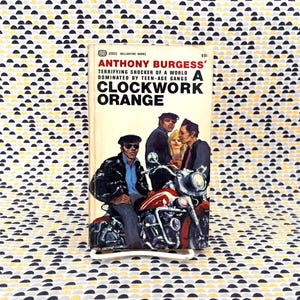 May include: A vintage paperback copy of Anthony Burgess's "A Clockwork Orange". The cover shows a motorcycle and three men. The book has a cream-coloured cover with black and red text and illustrations.
